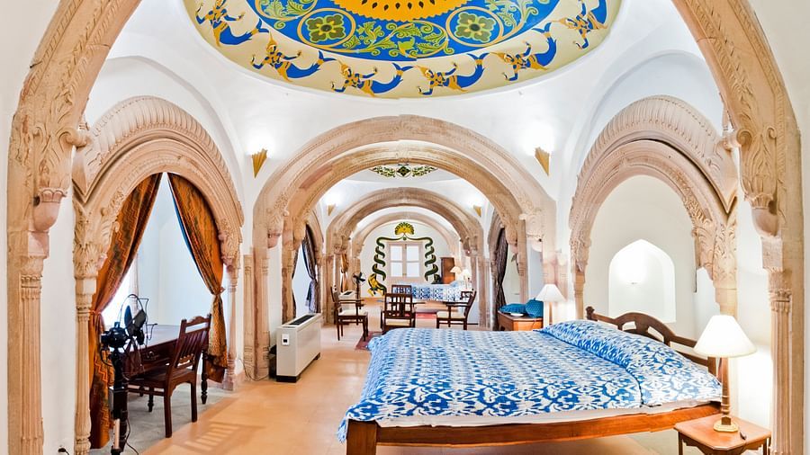 Room with bed, patterned bedding, arched doorways, decorated ceiling, furniture including desk and chairs, and curtains - Tijara Fort-Palace - 19th Century, Alwar.