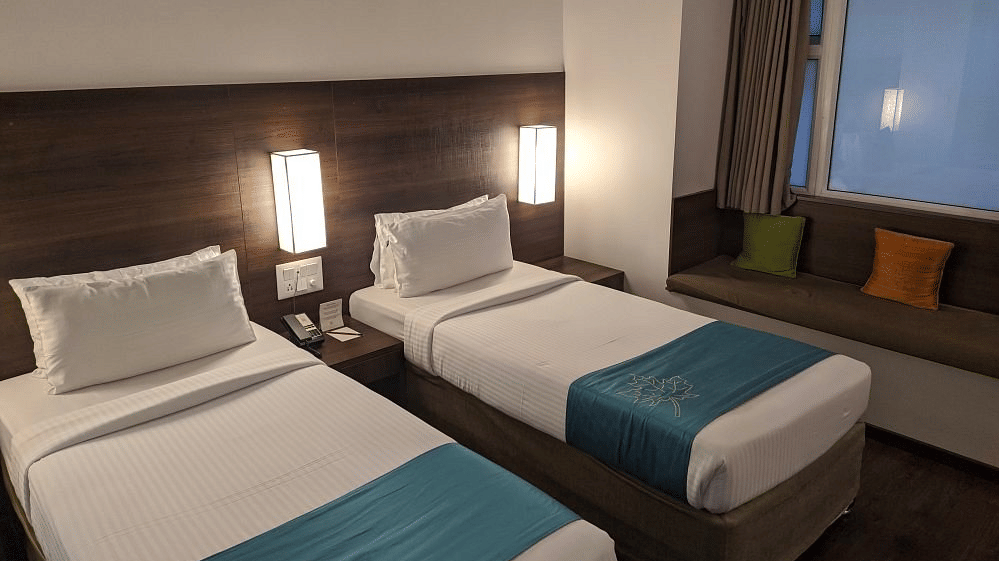 The Comfort Room at Temple Tree Hotel, Bangalore showcasing twin beds, a wooden head board, overhead lamps, and a large glass window.