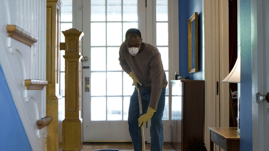 A view of a person holding a mop and cleaning the floor of a narrow hallway.