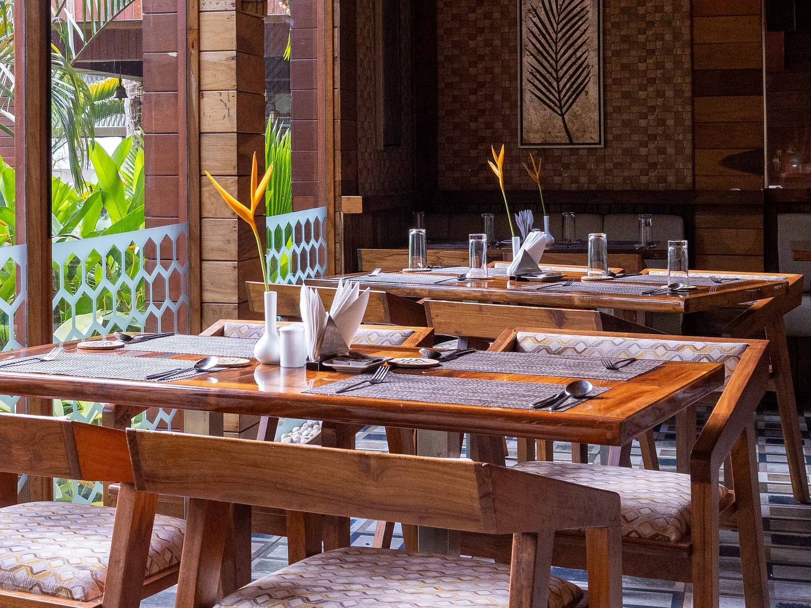 A spacious dining area at Ocean Prime with wooden tables and chairs, set in a modern wooden room. The decor is minimalist, with large windows offering a glimpse of the outside greenery - Coral Reef Resort & Spa, Havelock