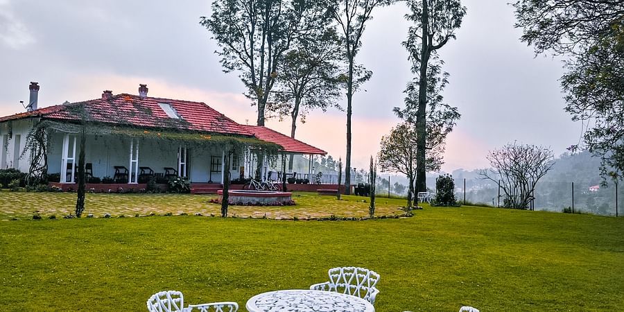 An overview of a lawn area with metal chairs and table and Ibex Stays & Trails, Coonoor (Leewood) in the background.