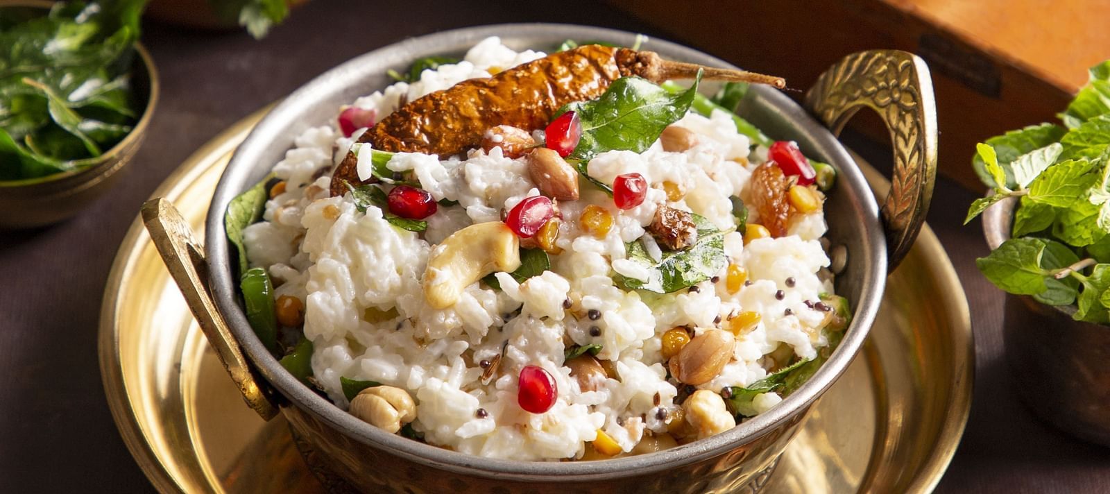 An image of a dessert garnished in a pot with pomegranate, dry fruits, and a chilly - Kamats India
