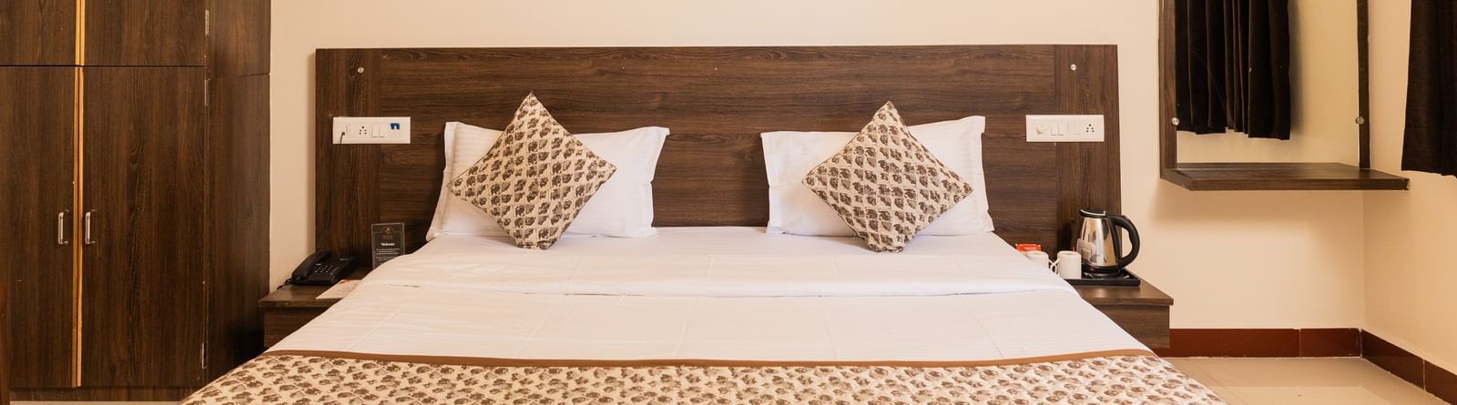 A view of the bed with brown accents, a wall art, a mirror reflecting the curtains, and a wooden wardrobe at Daksh Resort & Amusement Park, Sasan Gir.