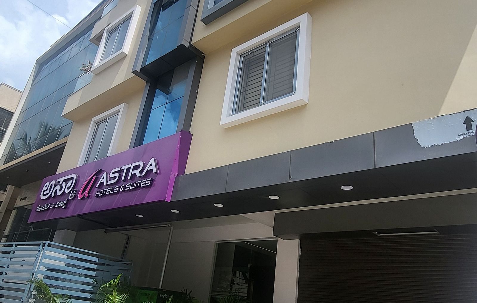 The exterior of a modern hotel building with multiple floors, large windows, and a bright blue sky in the background - Astra Hotels and Suites, HSR Sector 7
