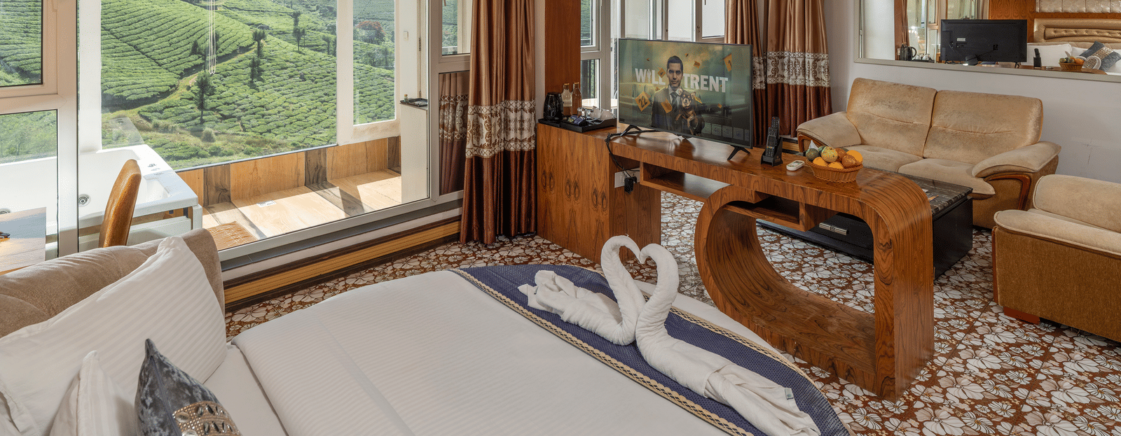 The interior of the Honey Moon Suite at Parakkat Nature Hotel and Resorts, Munnar, featuring a large bed, decorative wooden panelling, a ceiling fan, and glass windows overlooking the tea estates.