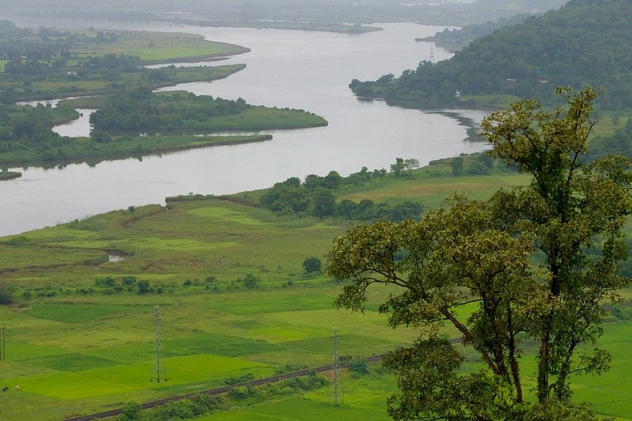 Overcast view from a high vantage point over a lush valley with a winding river cutting through dense green fields and distant hills shrouded in mist.