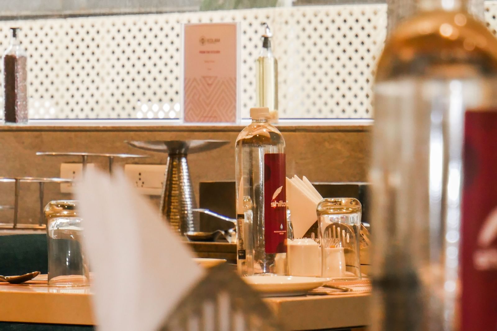 A blurred image showing a restaurant or bar area with warm lighting and various bottles at Shilton Dee Cee.