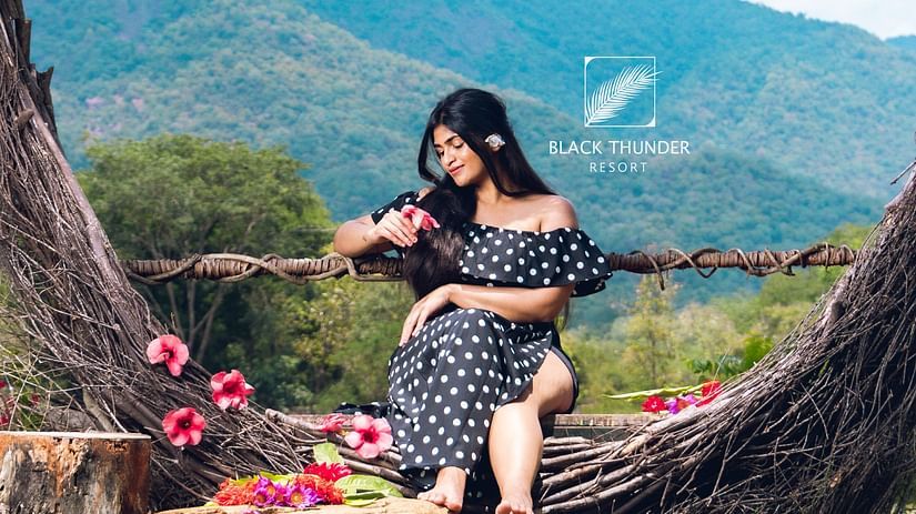 A woman sitting on a tree-formed heart-shaped seat in a scenic outdoor setting, surrounded by mountains and greenery - Black Thunder, Coimbatore