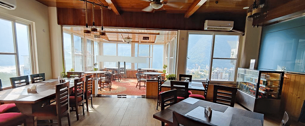 A spacious dining area with wooden flooring and several wide windows at Regenta Inn DLS.