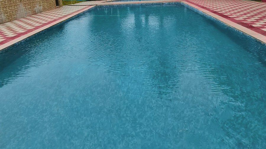 A close-up view of a large, rectangular swimming pool with bright blue water and a reddish-brown tiled border | Nandan Resort