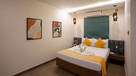 A side view of the room showcasing the bed, warm lighting, wall decor, and a large window offering natural light at Hotel Kyzen Smartstays – Smart, Reliable, Kyzen