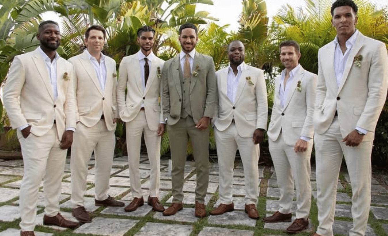 A group of groomsmen in beige suits standing outdoors on a stone pathway with greenery in the background | A Stone's Throw Away