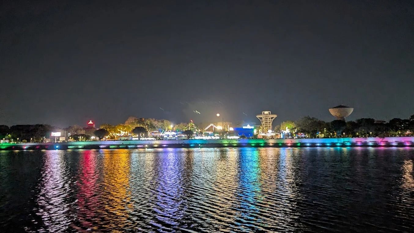 Night view of a brightly lit waterfront with colourful lights reflecting on the calm water, showcasing a lively promenade or lakeside area under a clear, dark sky.