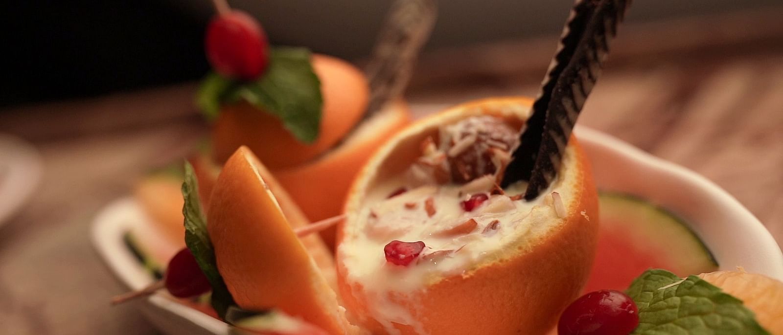 An image of a dessert served in a bowl along with orange, cherries, and mint leaves - Pai Group of Hotels