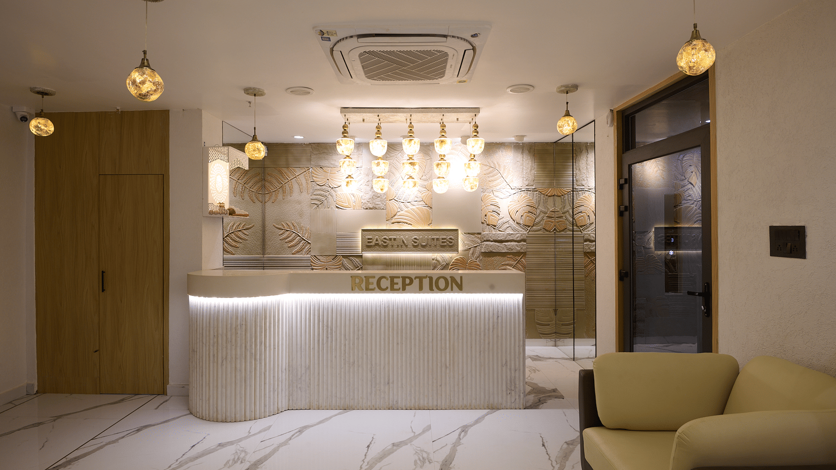 A hotel reception area with a curved white counter, pendant lighting hanging above the counter, and modern marble flooring | Voyage Eastin Suites