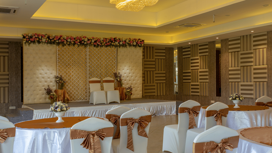 A brightly lit indoor banquet hall or reception area with tables and chairs set up, featuring elegant decor and a patterned wall - Grande Bay Resort & Spa, Mamallapuram