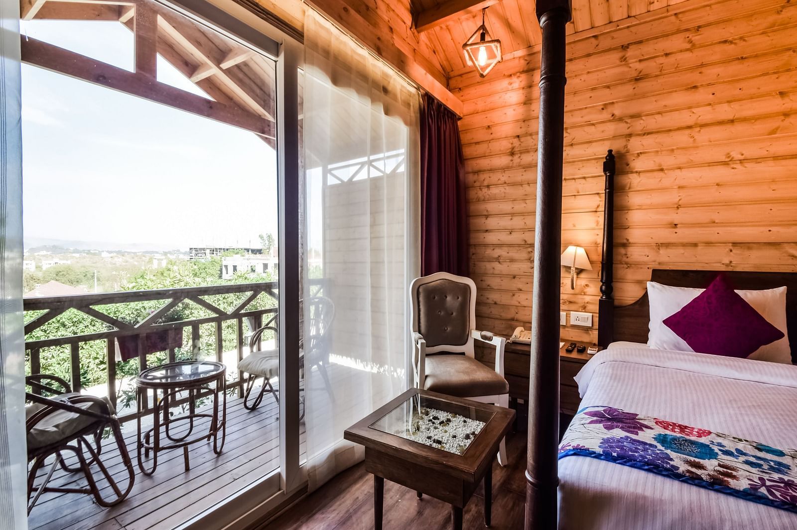  A cosy hotel room with wooden walls, a bed, and a balcony overlooking a scenic view. - Bamboo Saa Resort & Spa, Udaipur