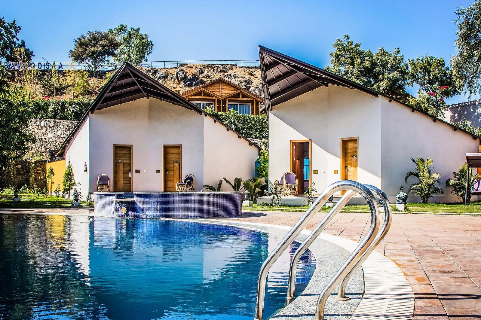 Two modern bungalows with pointed roofs flank a swimming pool.