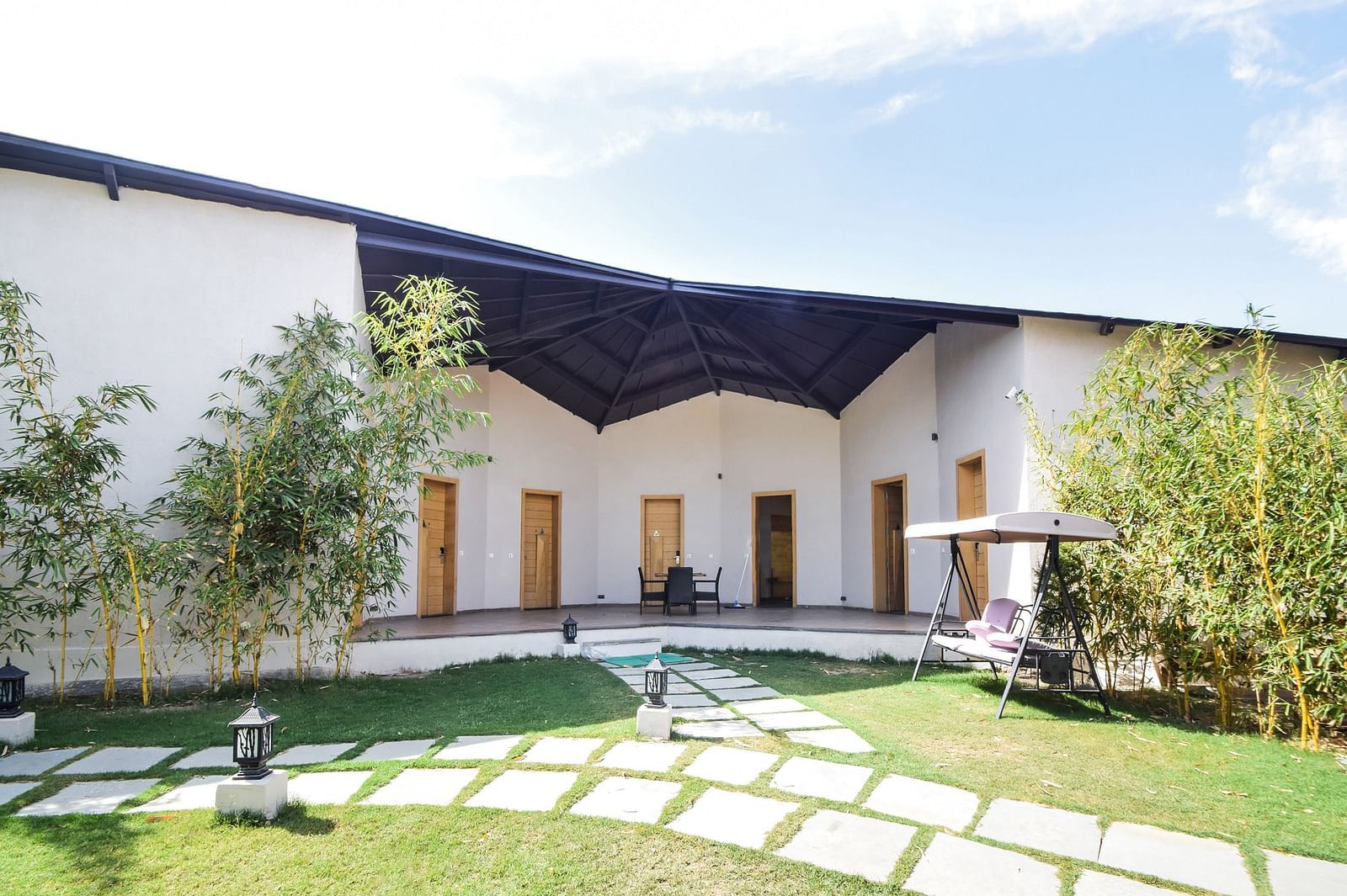 A building with a dark awning overlooks a grassy courtyard with a stone pathway. - Bamboo Saa Resort & Spa, Udaipur