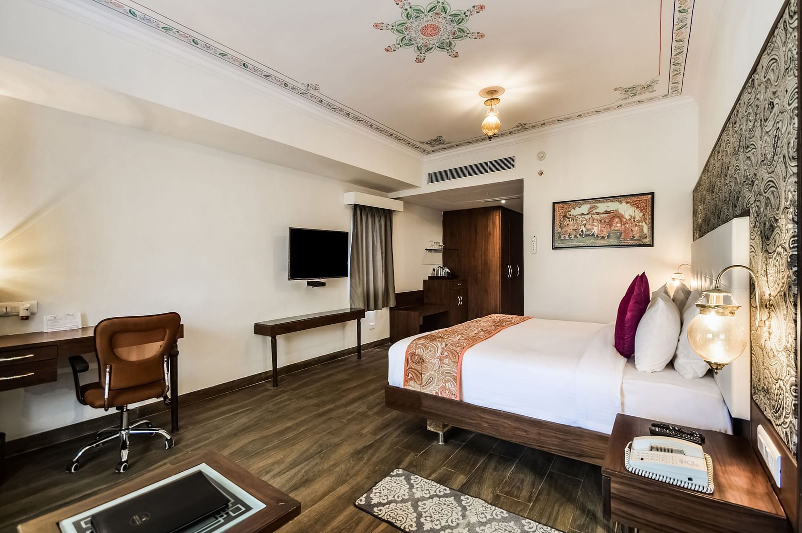  A hotel room with a large bed, a desk, and a seating area with warm lighting.- Bamboo Saa Resort & Spa, Udaipur
