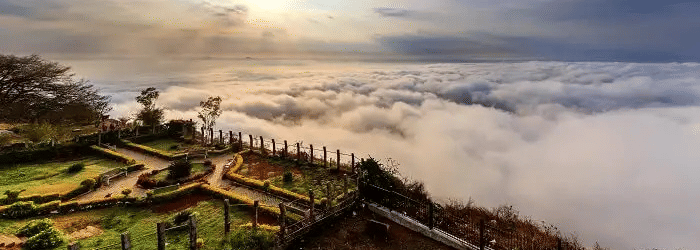 A panoramic shot of Nandi Hills in Bengaluru featuring amnucured garden overlooking a cloud covered landscape.