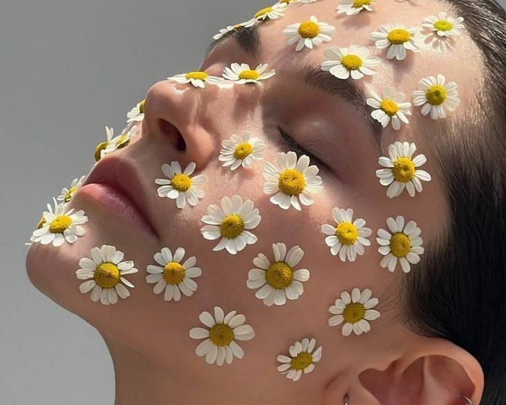 Woman’s face adorned with fresh chamomile flowers, highlighting natural skincare and relaxation.
