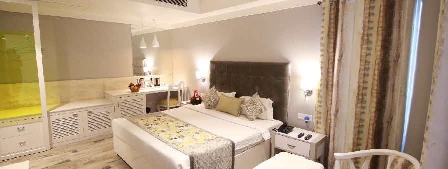 Elegant room with a large bed, table, chairs, cabinets, and TV unit at Hotel Emerald, Chandigarh