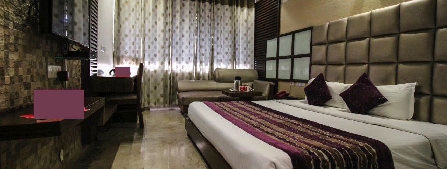 Elegant room with a large bed, table, chair, sofa and TV unit at Hotel Emerald, Chandigarh