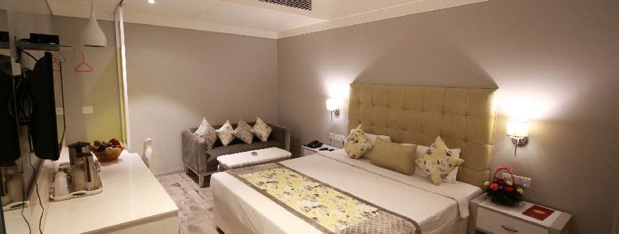 Elegant room with a large bed, bed side table, sofa, and TV unit at Hotel Emerald, Chandigarh