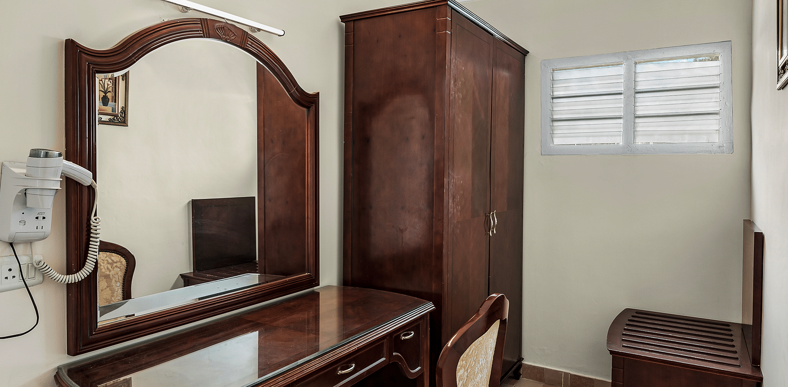 An image of the River View Room with balcony featuring a dressing table, chair, wardrobe with minimal decoration - GReaT Trails River View Resort Thanjavur By GRT Hotels
