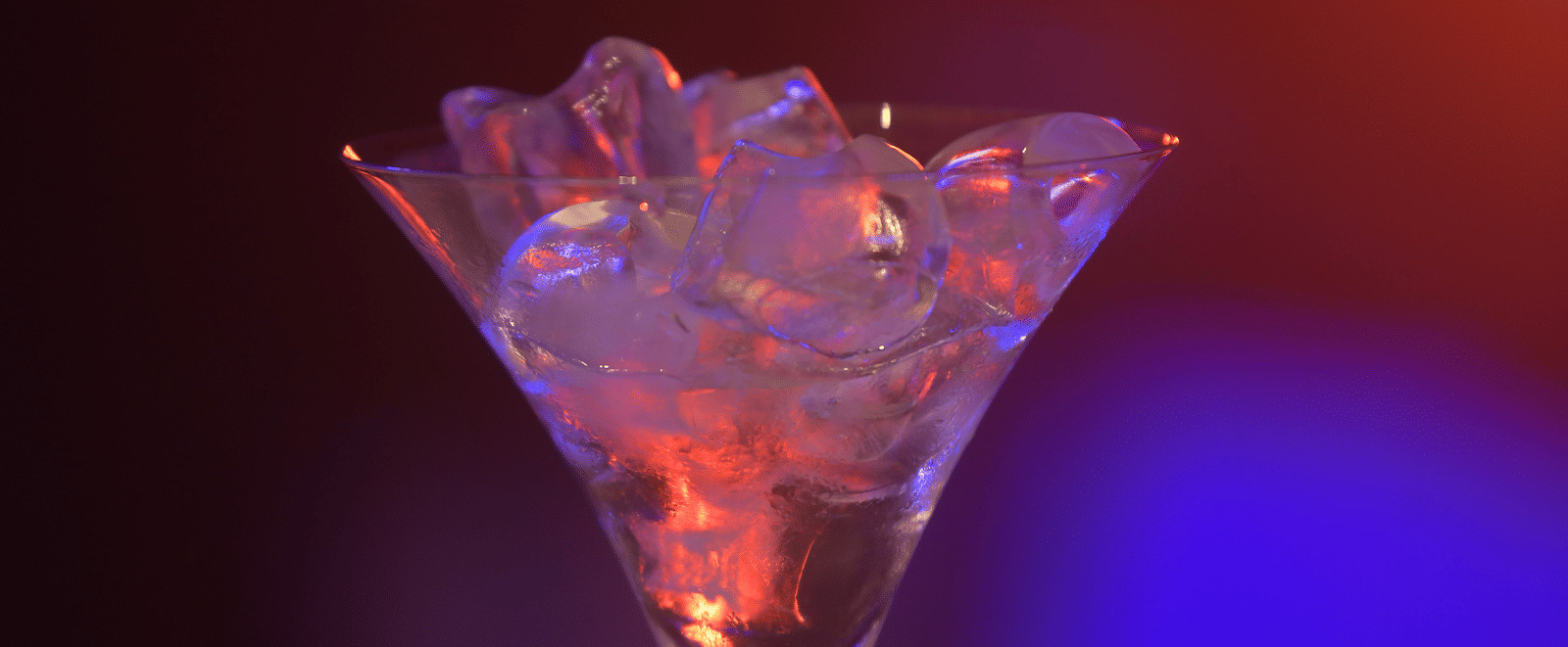 A martini glass filled with ice, glowing under warm orange and blue lighting at Hotel Sonar Bangla Mayapur.