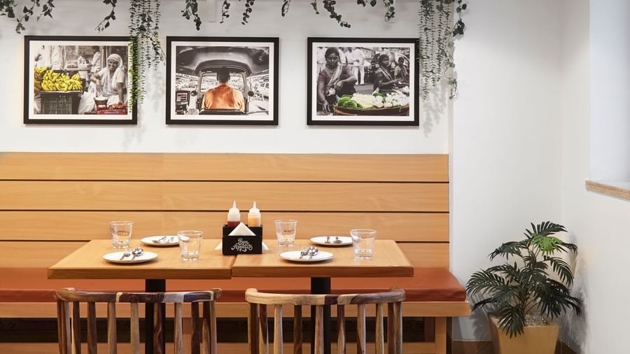 Another view of the dining space at Monday Hotels Mahape, Navi Mumbai, showing multiple wooden tables and seating arrangements.