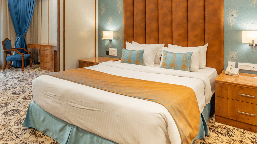 King size bed with blue and orange accents, a large, tufted orange headboard, and ornate patterned carpet at Hotel Hukam's Lalit Mahal.
