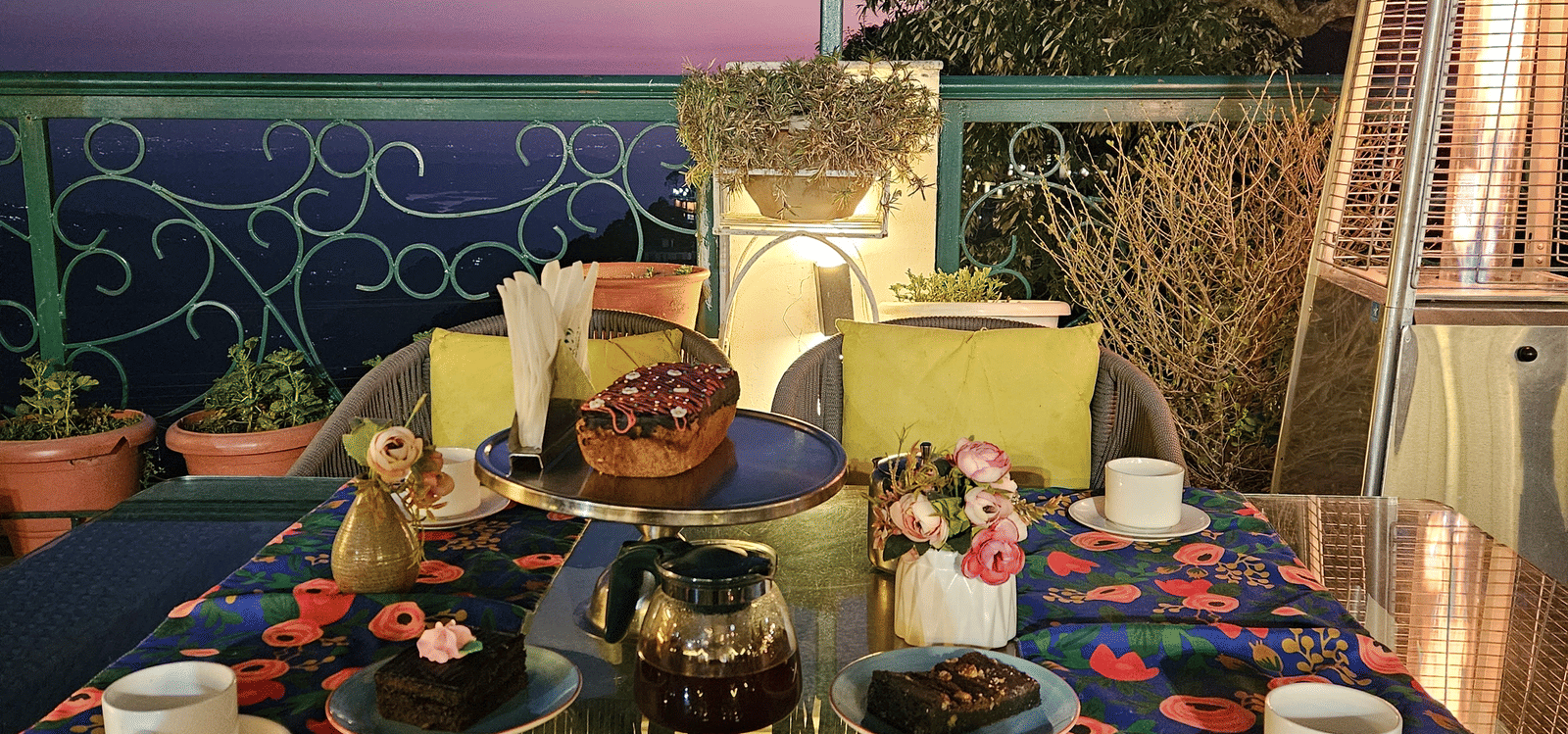 A terrace with tables set for dining under ambient lighting, offering sunset views at Mongas Hotel & Resort, Dalhousie.