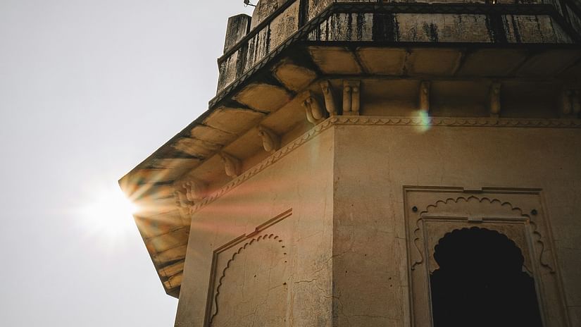 A historic watchtower with intricate architecture, illuminated by sunlight against a clear sky.