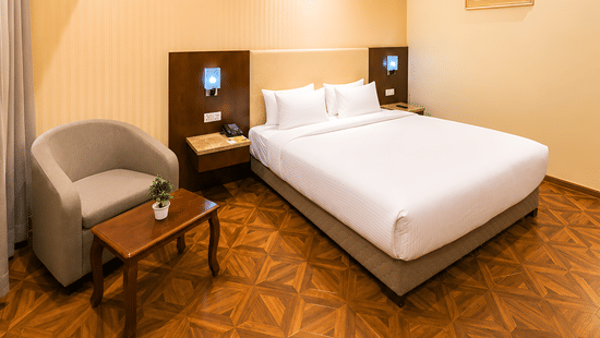 Compact view of the Deluxe room at Golden Tulip Kukas Jaipur with a king bed, armchair in the corner, patterned carpet, and warm ceiling lighting