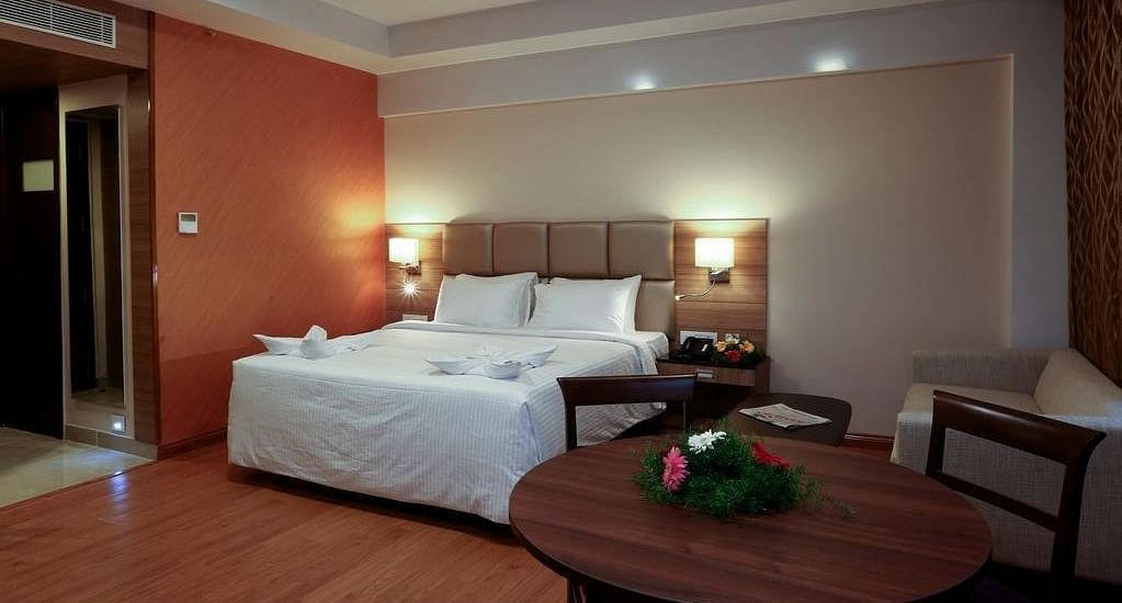 Room with bed and a table with flowers on top at Fressotel Seetharam, Coimbatore