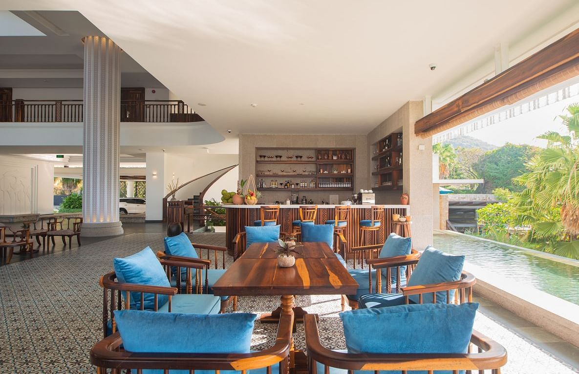 A restaurant with wooden furniture for sitting and a serene view of the pool through a glass door - Alibu Resort Nha Tarng