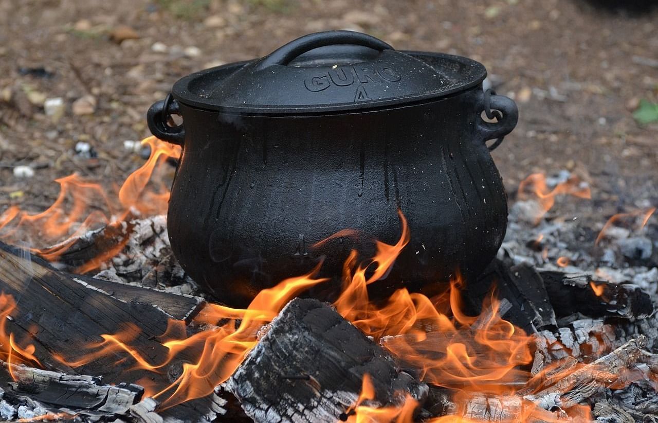 A black cast iron pot cooking on a burning flame.