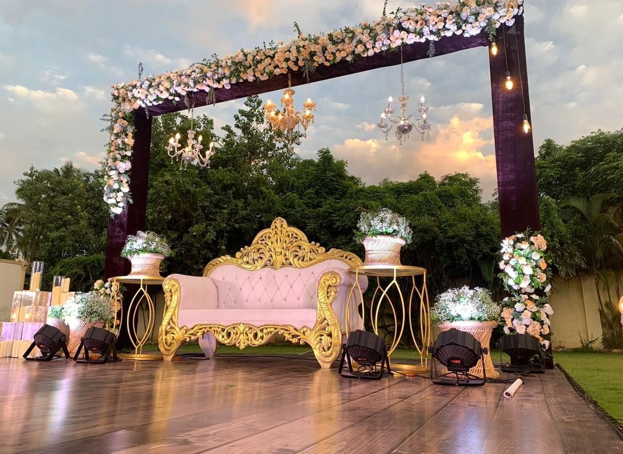 Decorated stage with golden sofa and floral canopy setup for a celebration at Ilara Hotels & Spa, OMR, Chennai