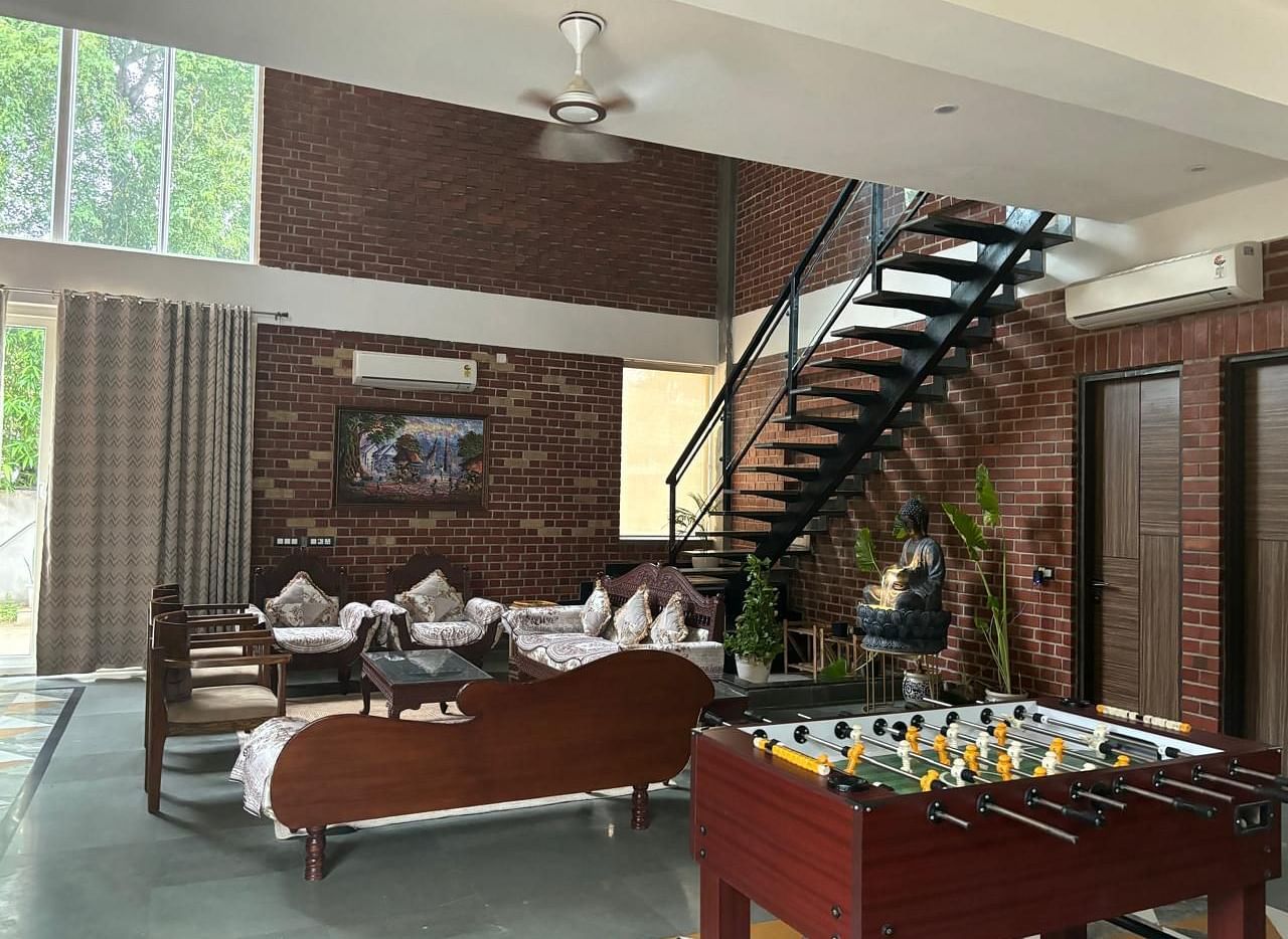 A well-lit living room with a modern interior, featuring a foosball table, comfortable seating, and a staircase leading to an upper level.