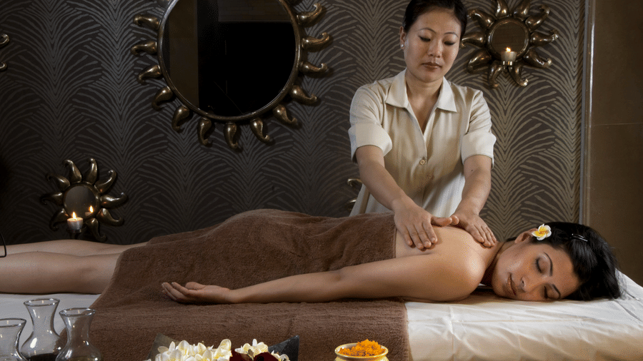 A guest lying on a spa bed receiving a massage from a therapist at Heritage Village Resorts & Spa, Manesar.