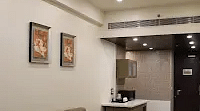 A cozy space with a plush couch and 2 artwork framed on the wall with a small table beside. - Golden Suites, Gurgaon