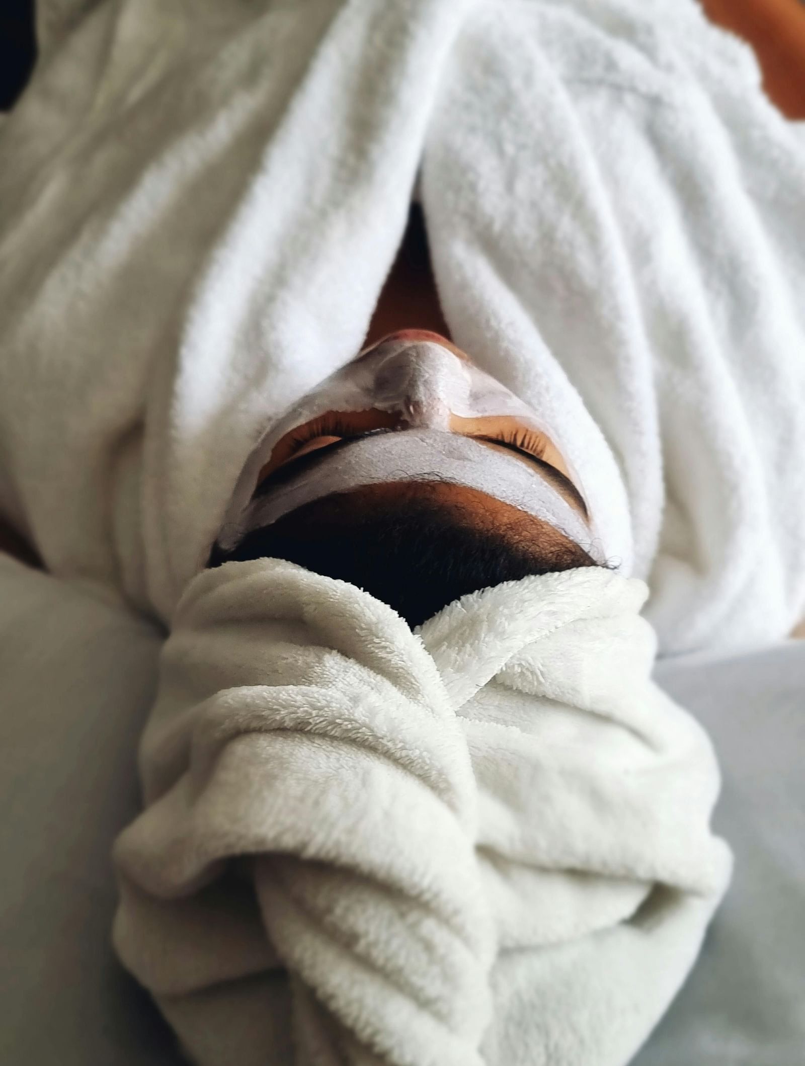 A person laying wrapped in a white towel with a face mask on.