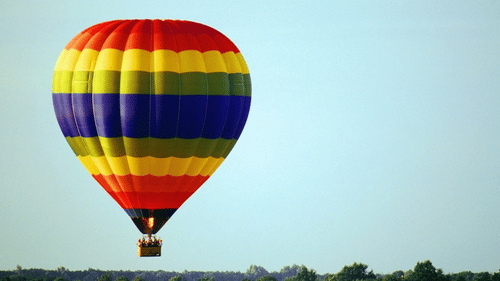 A colourful Hot Air Balloon Coimbatore with vibrant stripes of red, yellow, green, and blue, floating against a clear sky