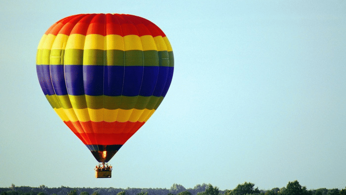 A colourful Hot Air Balloon Coimbatore with vibrant stripes of red, yellow, green, and blue, floating against a clear sky