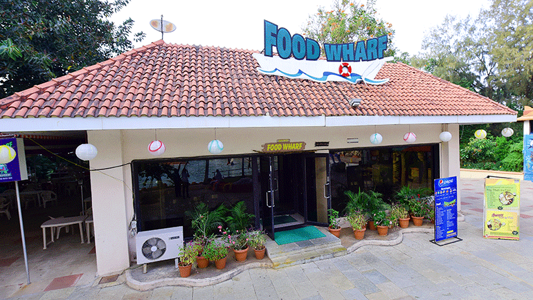 Facade of Food Wharf, a restaurant in Water Kingdom, featuring a red tiled roof with a sign board.