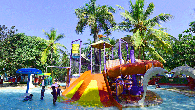 A view of the Goofers Lagoon at Water Kingdom with children playing on the pool and coconut and other trees in the background. Some of the best facilities at Water Kingdom are available for guests to enjoy the rides and the water.