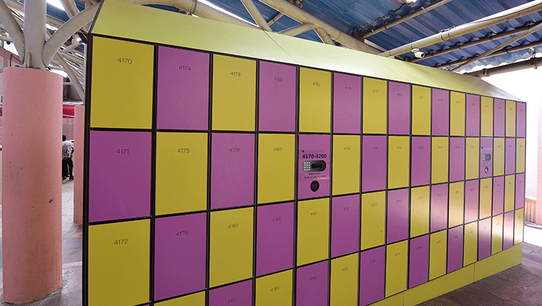 A large bank of bright yellow and purple storage lockers stands under a covered shelter - Water Kingdom