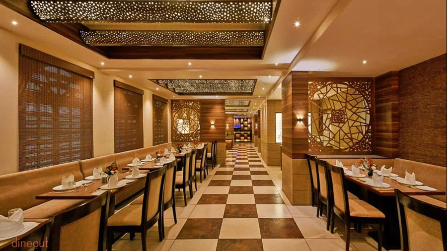 Restaurant interior with long rows of tables, chairs, checkered flooring, and ceiling lights.